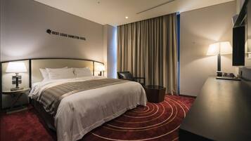 A hotel room with a bed, a desk, a chair, a lamp, and a sign on the wall.