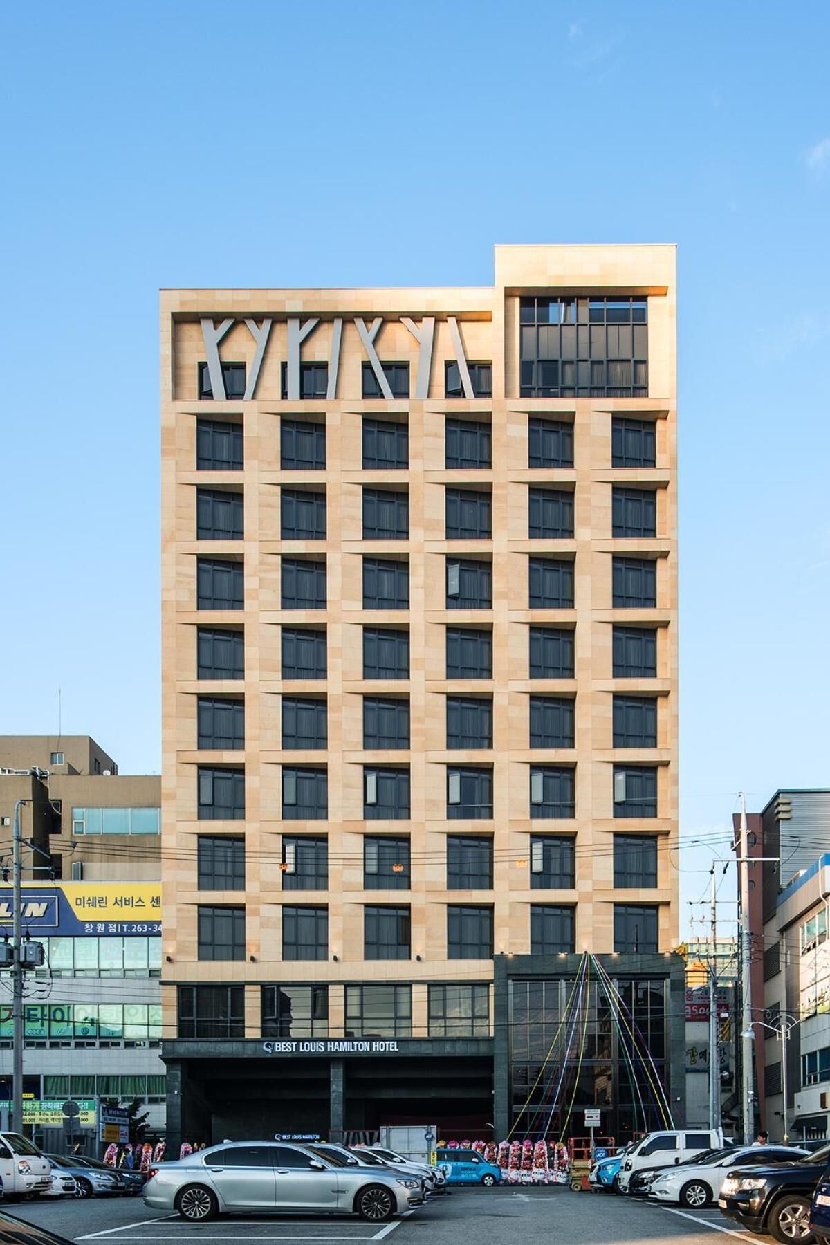 Un moderno edificio de hotel con un llamativo letrero 'KY' en la fachada, varios pisos y una vista despejada de la calle.