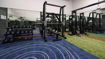 A gym with weightlifting equipment, a bench, and a mirror wall.
