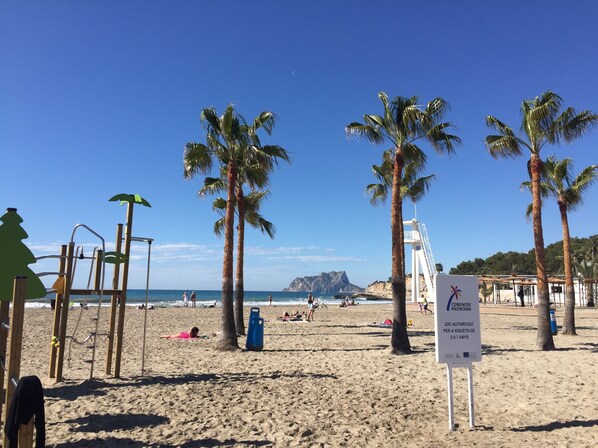 A beach with palm trees, a lifeguard tower, and a sign in the foreground. - Perfect private holiday hideaway (Teulada)
