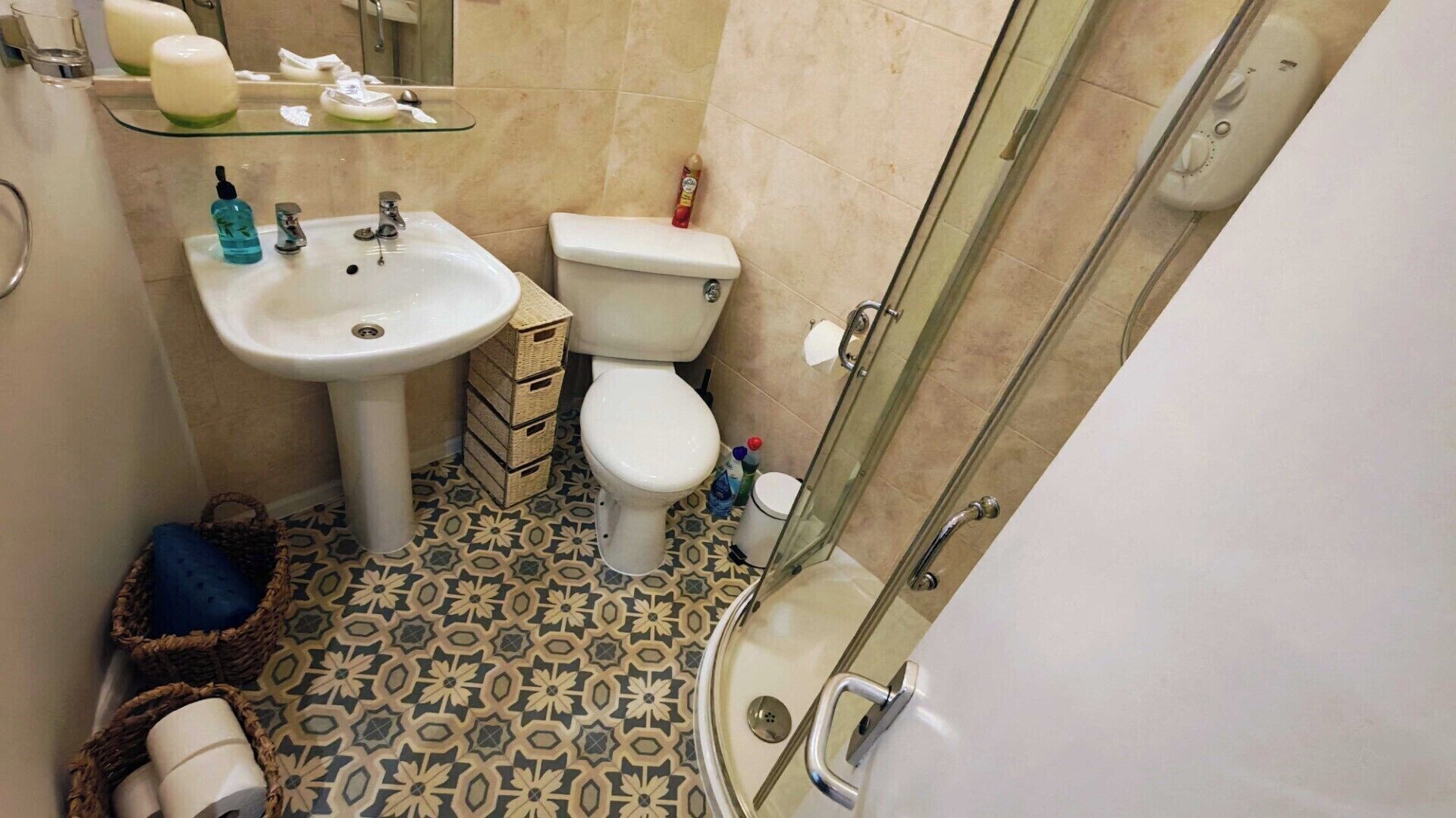 Un bany amb rentatge, vàter, dutxa i rajoles de terra amb un disseny decoratiu.