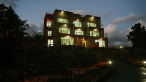 A modern multi-story building with large windows and balconies, surrounded by landscaped gardens and a pathway. - Oasis Pension (Seogwipo)