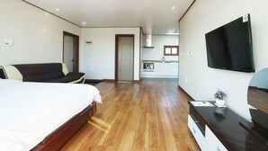 A hotel room with a bed, a sofa, a TV, and a kitchenette in the background. - Oasis Pension (Seogwipo)