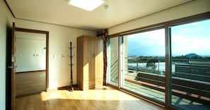 Une pièce dotée d’un plancher en bois, d’un porte-manteau, d’une porte et d’une grande porte-fenêtre coulissante donnant sur un balcon avec vue sur des immeubles et une colline lointaine.