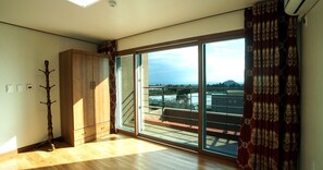 A room with a wooden wardrobe, a coat rack, and a large sliding glass door leading to a balcony with a view of buildings and a mountain. - Oasis Pension (Seogwipo)