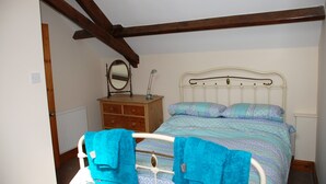 A bedroom with a bed, wooden beams, a dresser, a mirror, and towels.