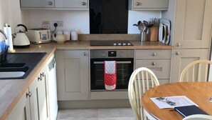 A kitchen with grey cabinets, a wooden countertop, a stove, a sink, and a dining table with chairs.