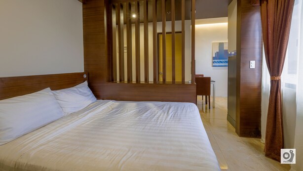A hotel room with a large bed, wooden headboard, and a view of the cityscape through a window. - Bed and Bath Serviced Suites (Iloilo)