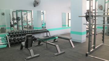 Un gimnasio con equipo de levantamiento de pesas, bancos y mancuernas.