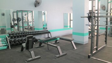 Un gimnasio con equipo de levantamiento de pesas, bancos y mancuernas.