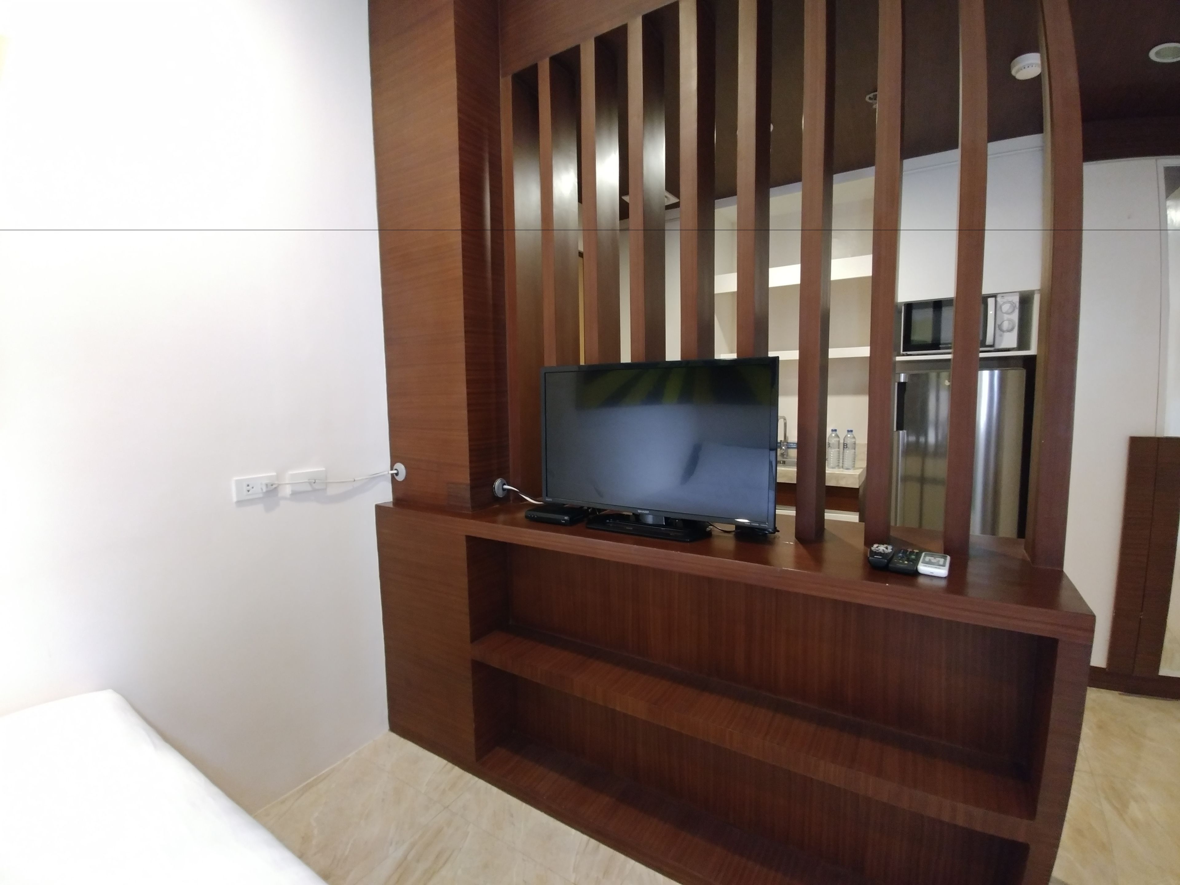 A wooden entertainment unit with a flat-screen TV, a remote control, and a power outlet.