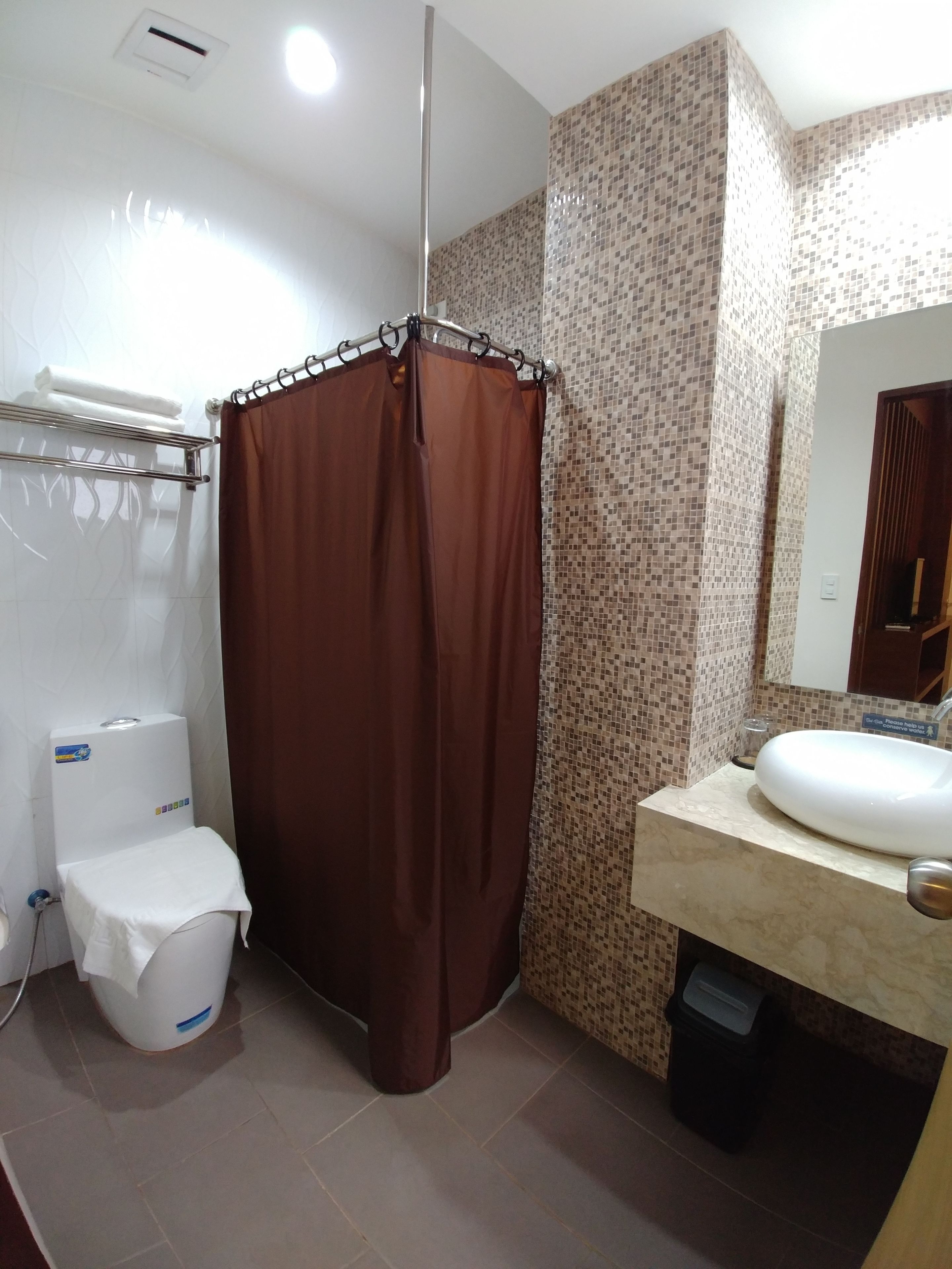 A bathroom with a shower curtain, toilet, sink, and tiled walls.