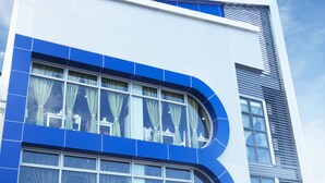 A modern building with a prominent 'B' logo, large windows, and a flag on top. - Bed and Bath Serviced Suites (Iloilo)