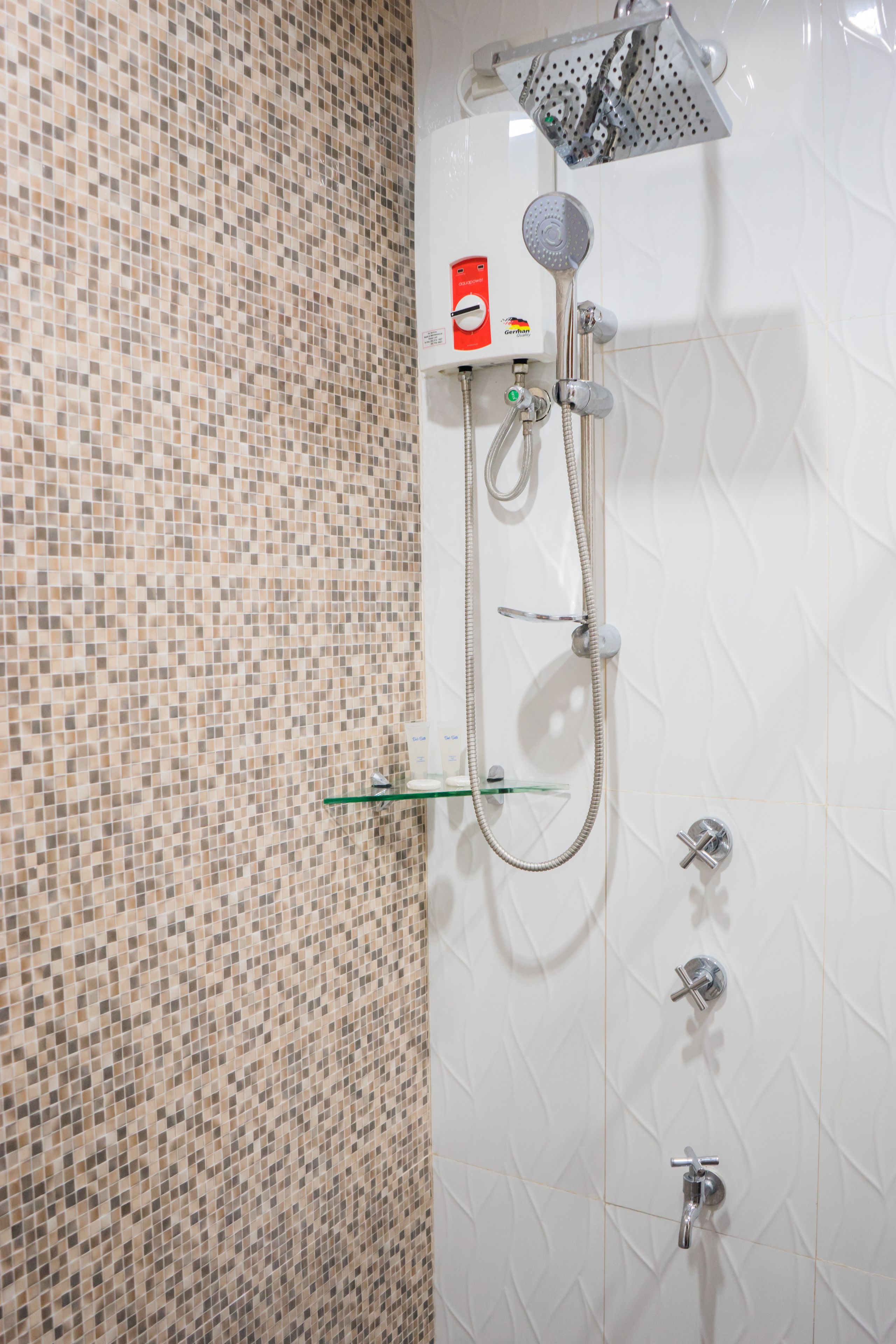 A bathroom with a mosaic tile wall, a showerhead, and a handheld shower attachment.
