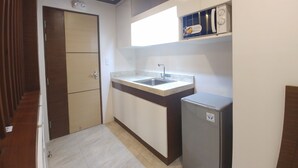 A compact kitchen with a built-in sink, a small refrigerator, and a wooden door. - Bed and Bath Serviced Suites (Iloilo)