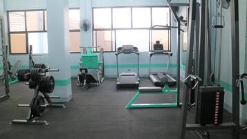 Une salle de sport équipée de matériel de musculation, de tapis de course et d’un tapis d’exercice vert.