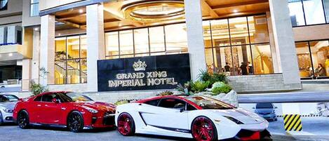 The Grand Xing Imperial Hotel with two luxury sports cars parked in front.