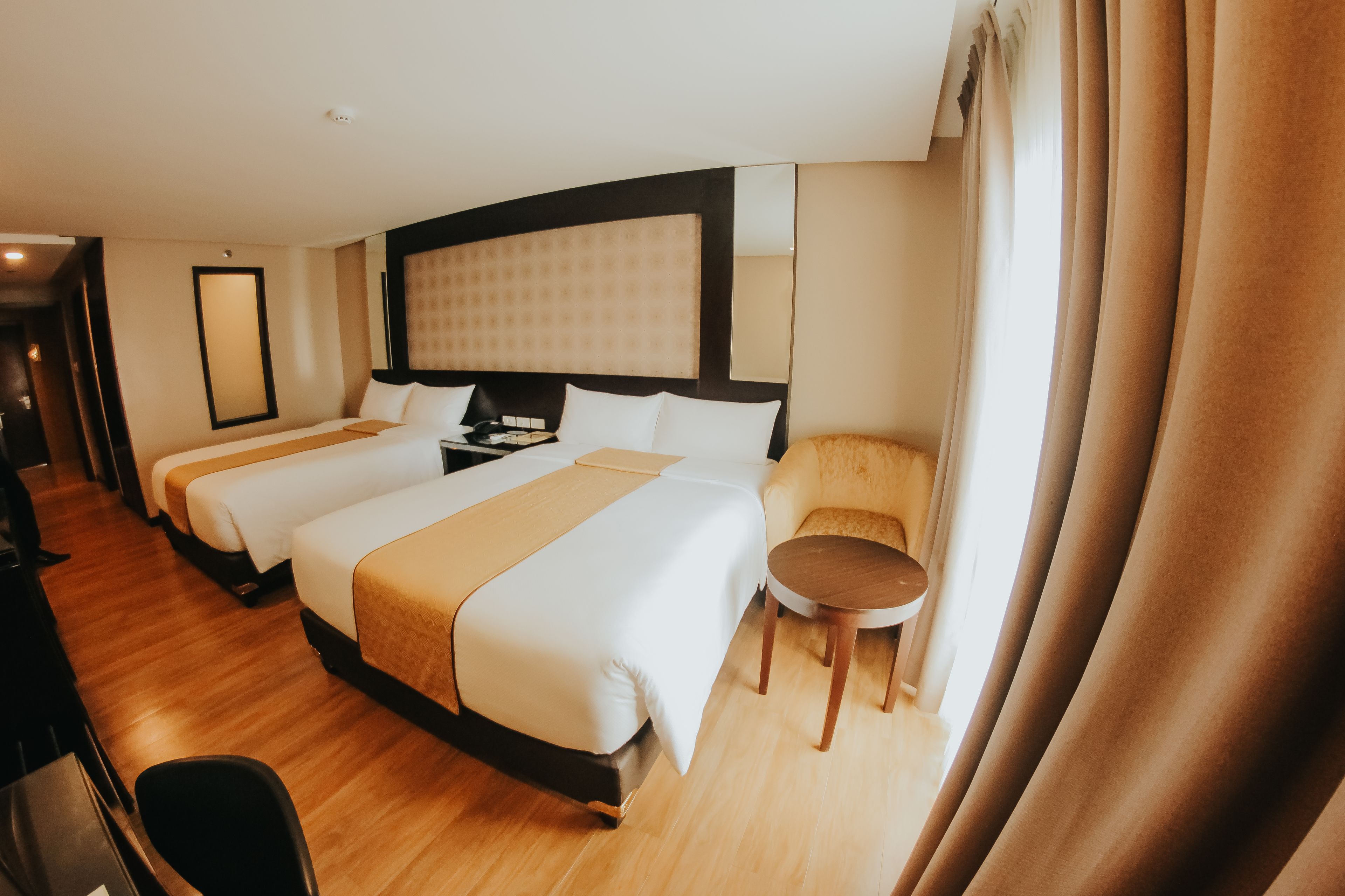 A hotel room with three beds, a desk, a chair, and a small table.