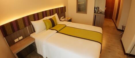 A hotel room with a large bed, bedside table, and a mirror. There is a desk with a chair and a small kitchenette in the corner.