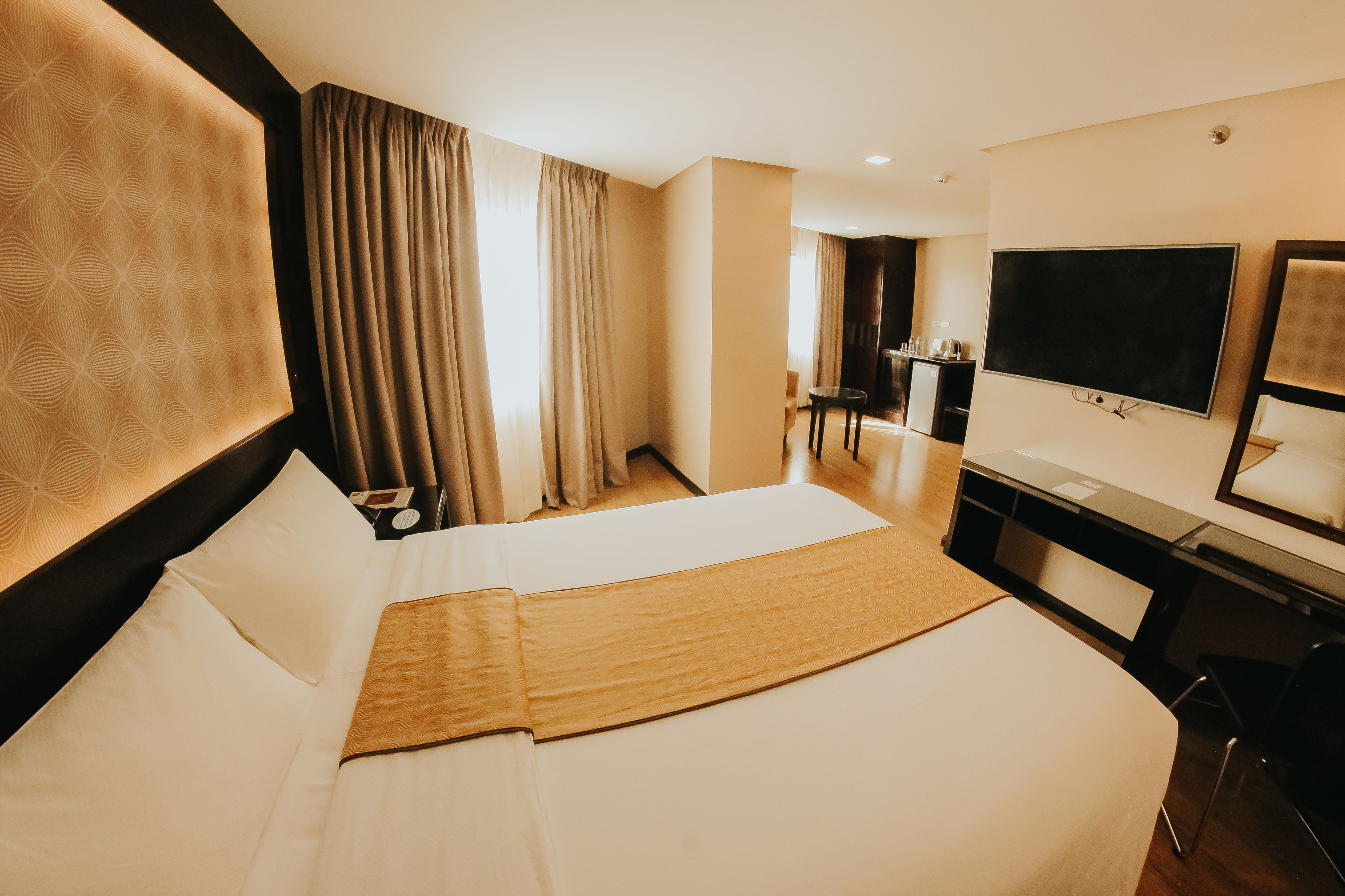 Een hotelkamer met een groot bed, een bureau, een televisie en een badkamer op de achtergrond.