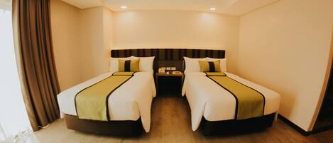 A hotel room with two single beds, a large window with curtains, a wooden floor, and a dark headboard.