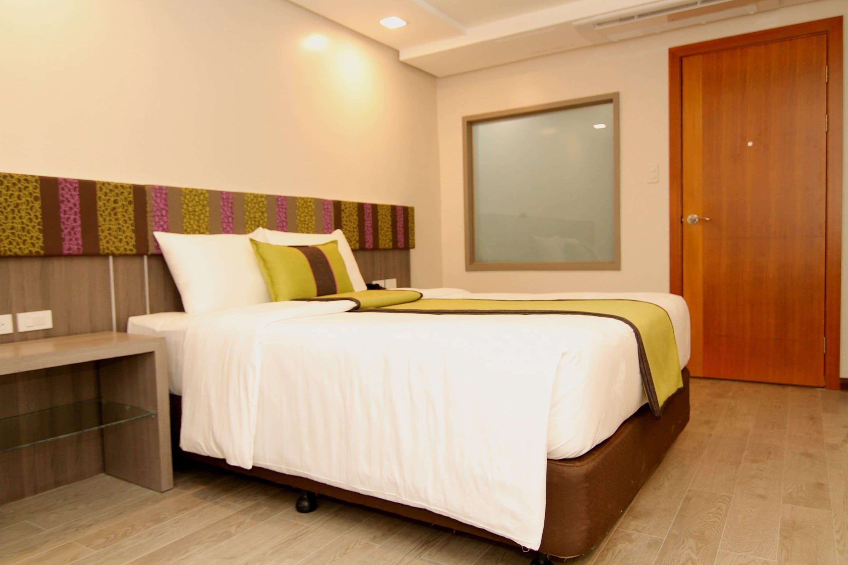 Una habitación de hotel moderna con una cama, una mesita de noche y un ventanal grande.