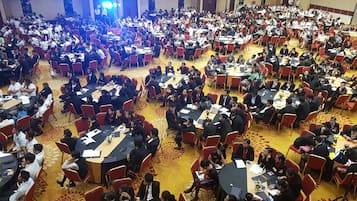 Un salón de conferencias amplio con varias mesas redondas y sillas rojas, dispuesto en una distribución espaciosa.
