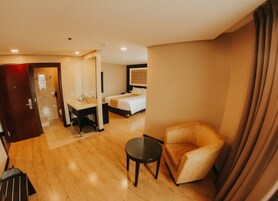 Una habitación de hotel con cama, escritorio con silla, una mesita y un sofá.