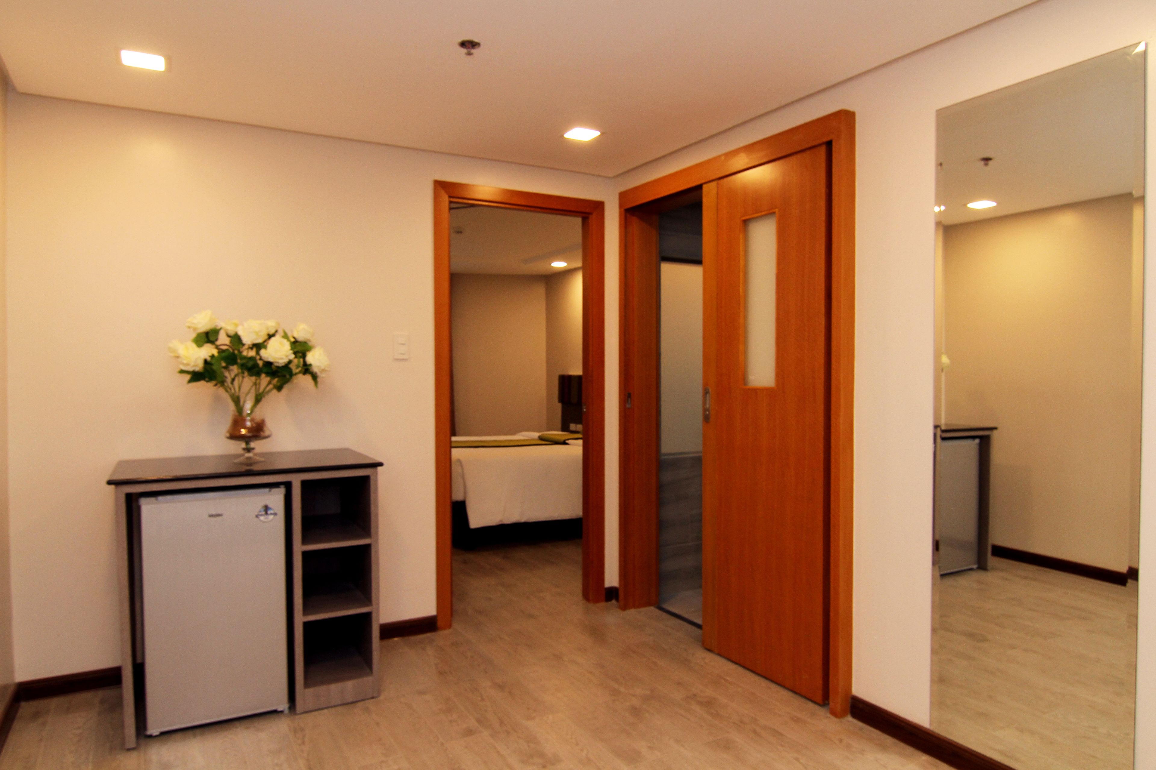 A hotel corridor with a minibar, a bed, and a wooden door.