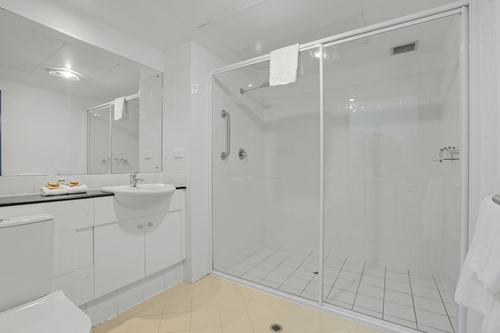 Un baño moderno con ducha envuelta en vidrio, lavamanos blanco y un espejo grande.