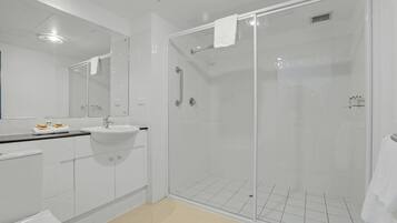 Un baño moderno con ducha envuelta en vidrio, lavamanos blanco y un espejo grande.