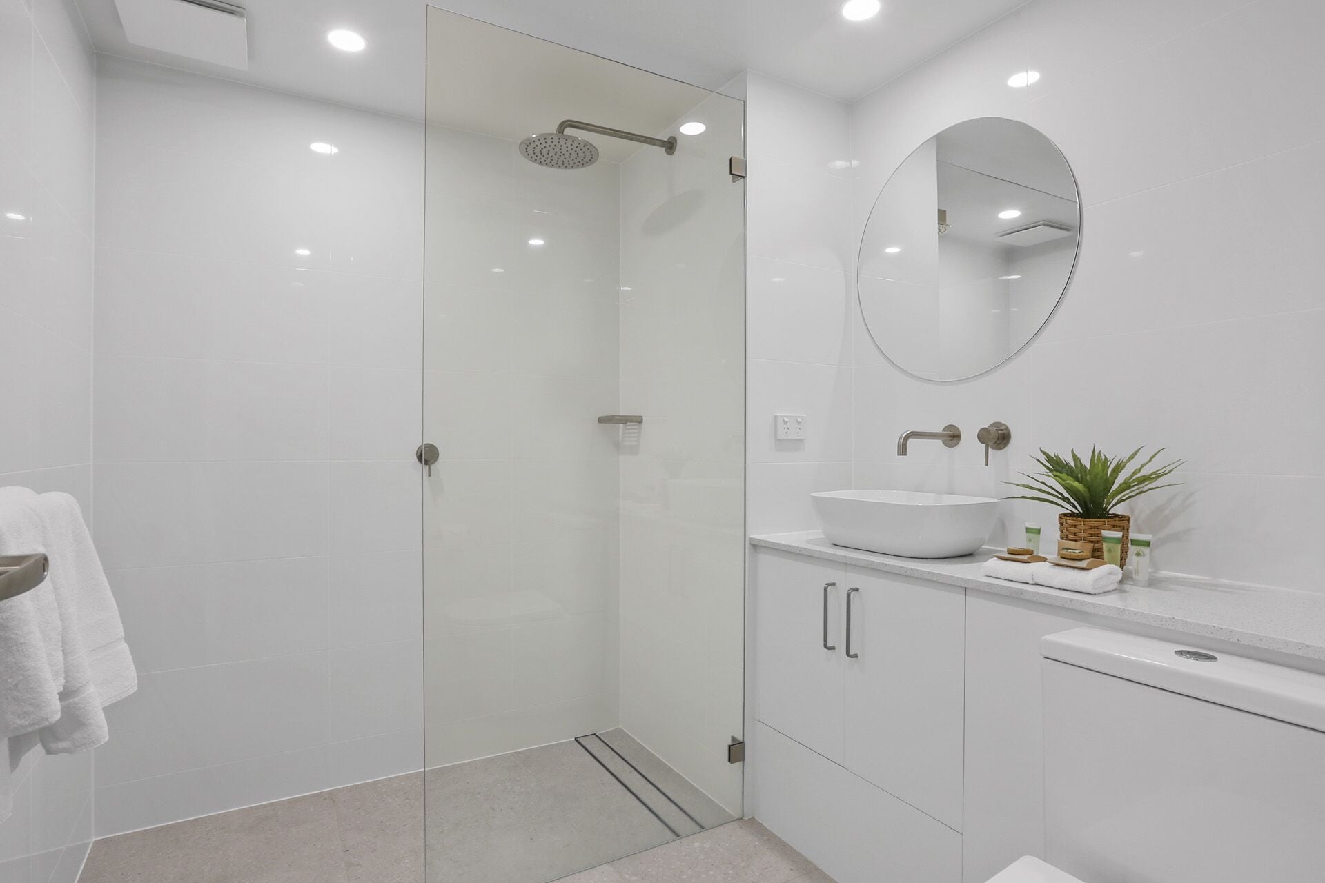 Un baño moderno con ducha de vidrio, espejo redondo y lavamanos blanco.