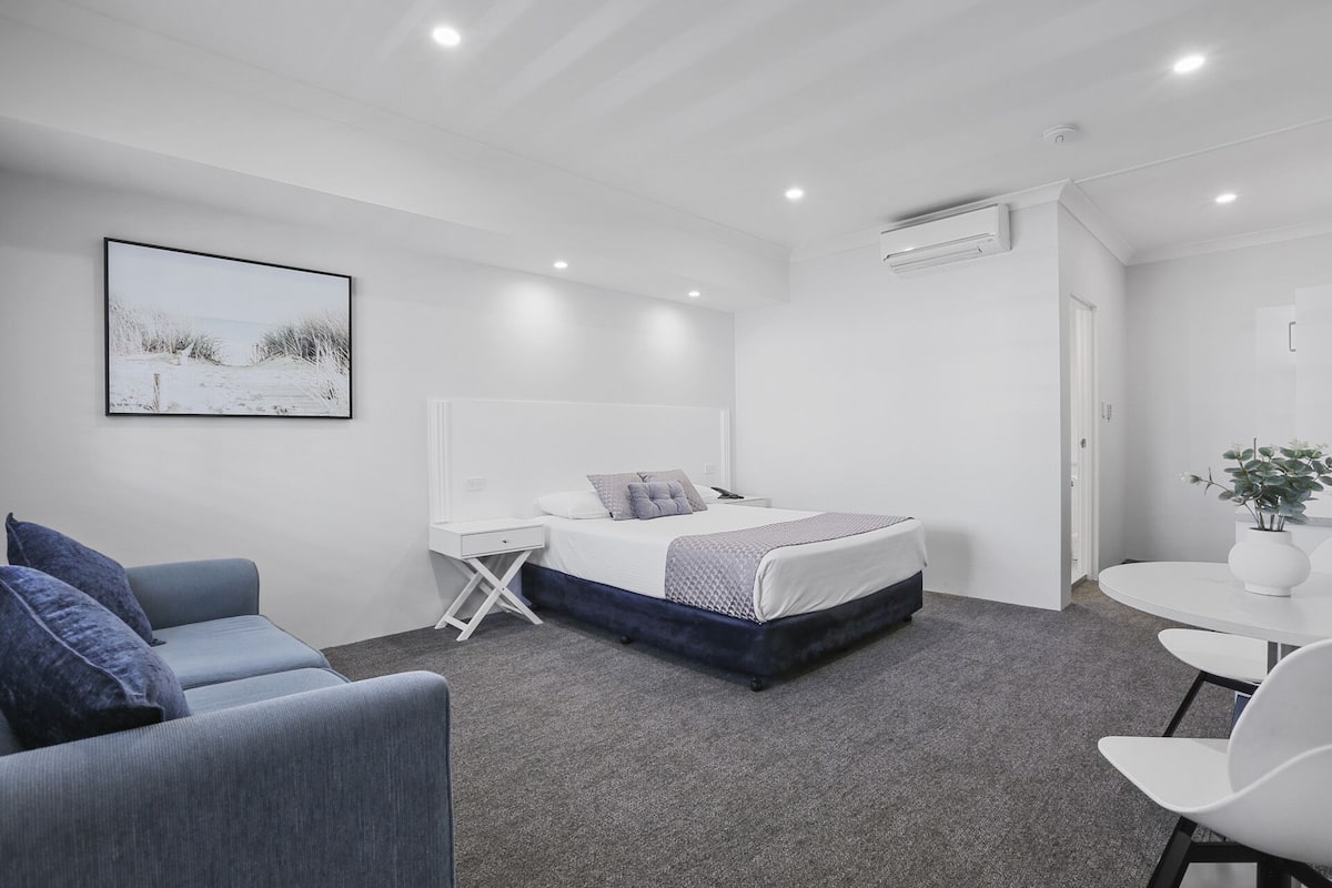 Un dormitorio moderno y minimalista con cama, mesita de noche y un pequeño escritorio.