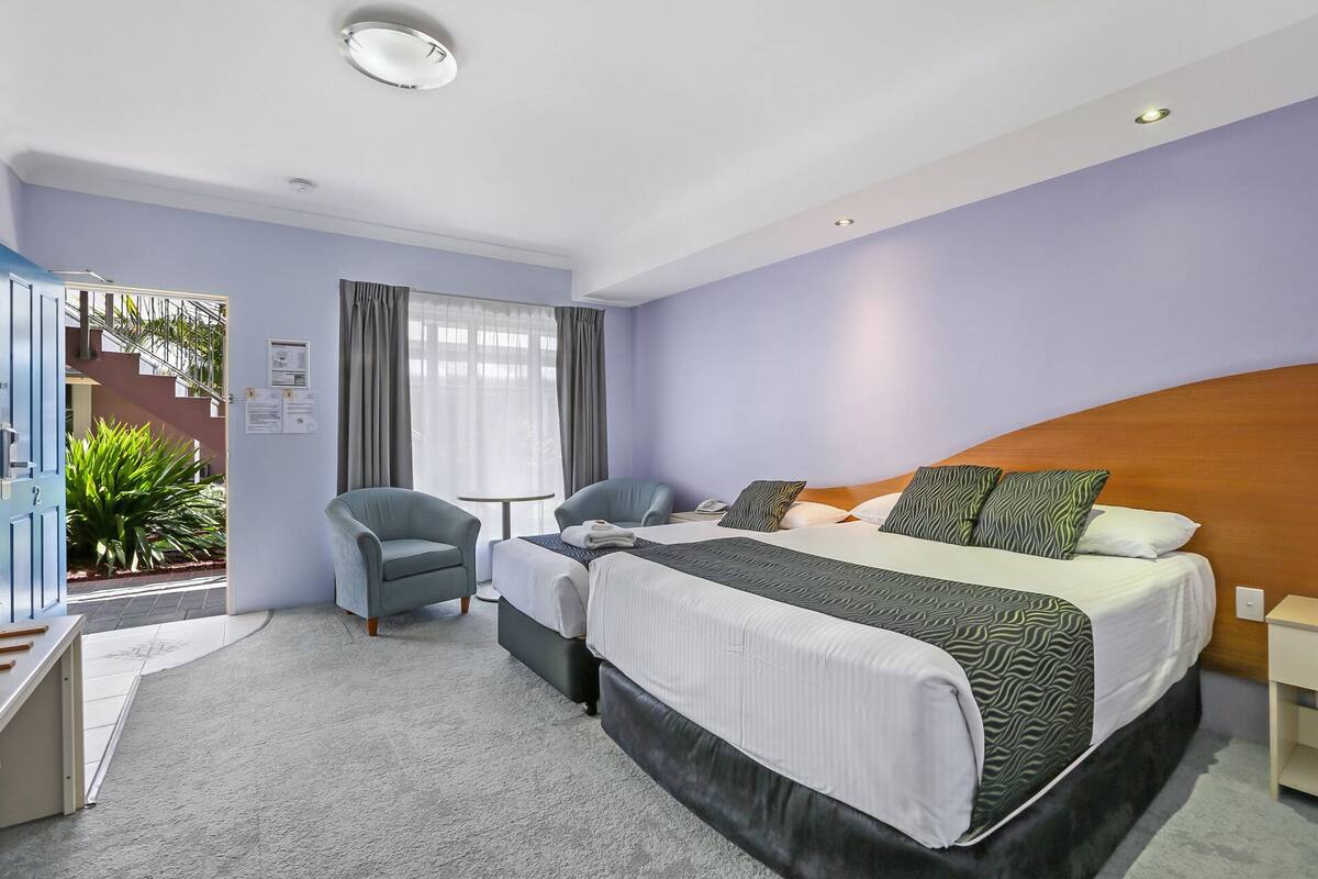 Una habitación de hotel con una cama, dos sillones, una mesita y una escalera que lleva a un espacio exterior.