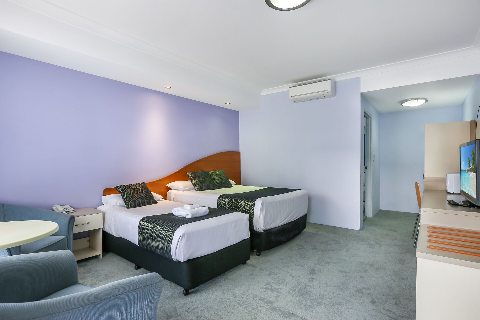 A hotel room with two beds, a desk, a chair, and a television.