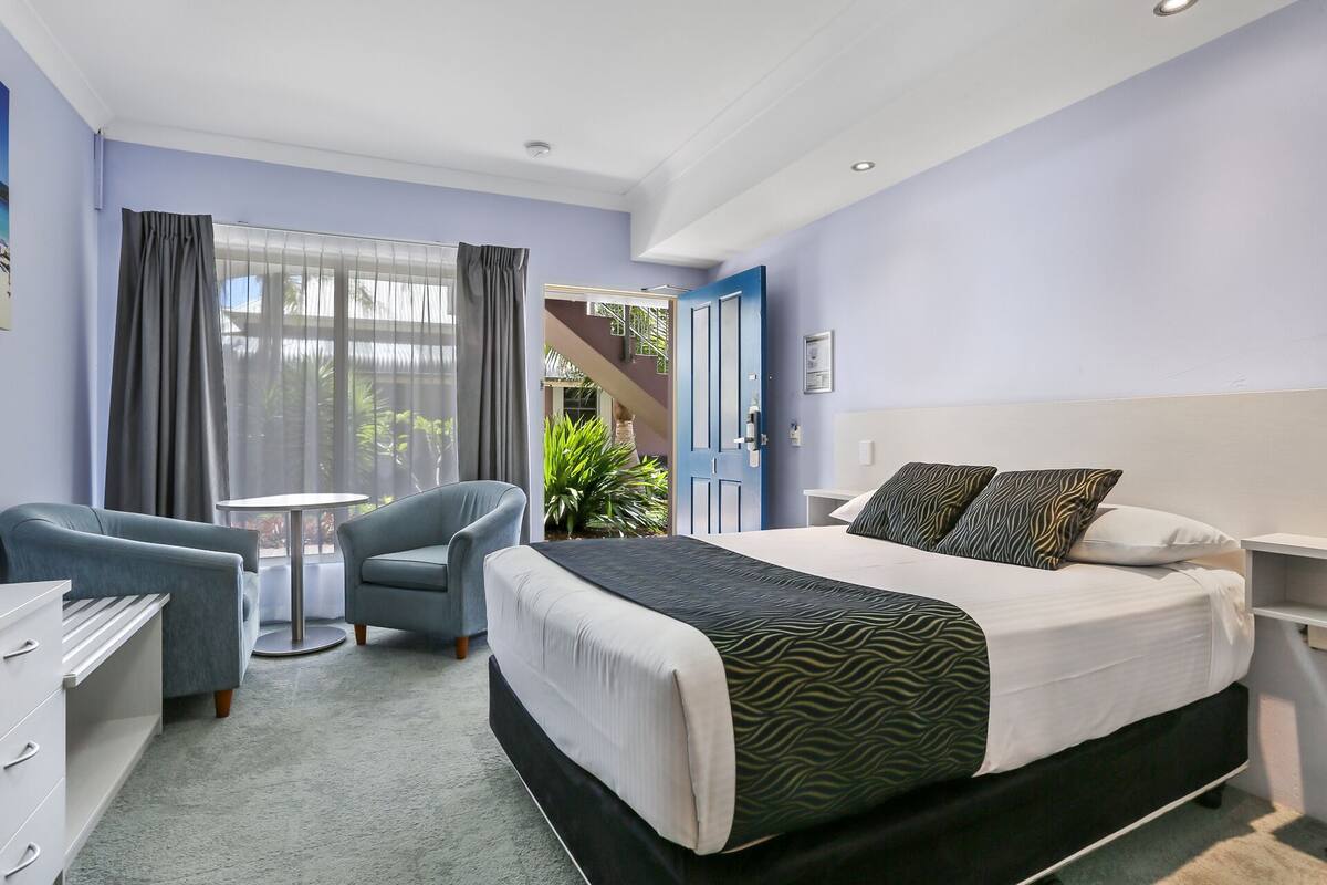 Habitación de hotel con cama, sillón, escritorio y vistas al exterior.
