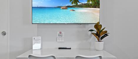 A reception desk with a TV displaying a beach scene, a no-smoking sign, a plant, and a sign indicating complimentary milk.