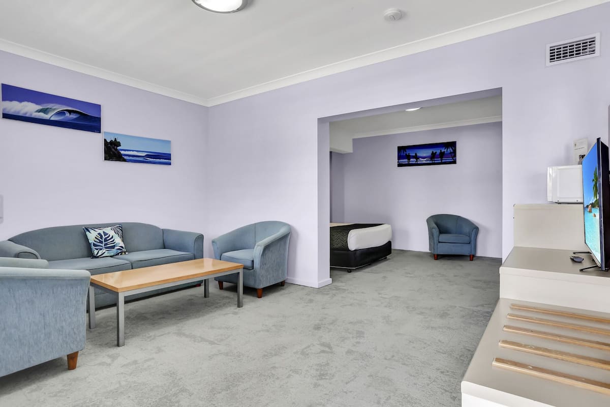 Una sala moderna con un sofá gris, una mesa de centro de madera y un televisor sobre un mueble bajo.