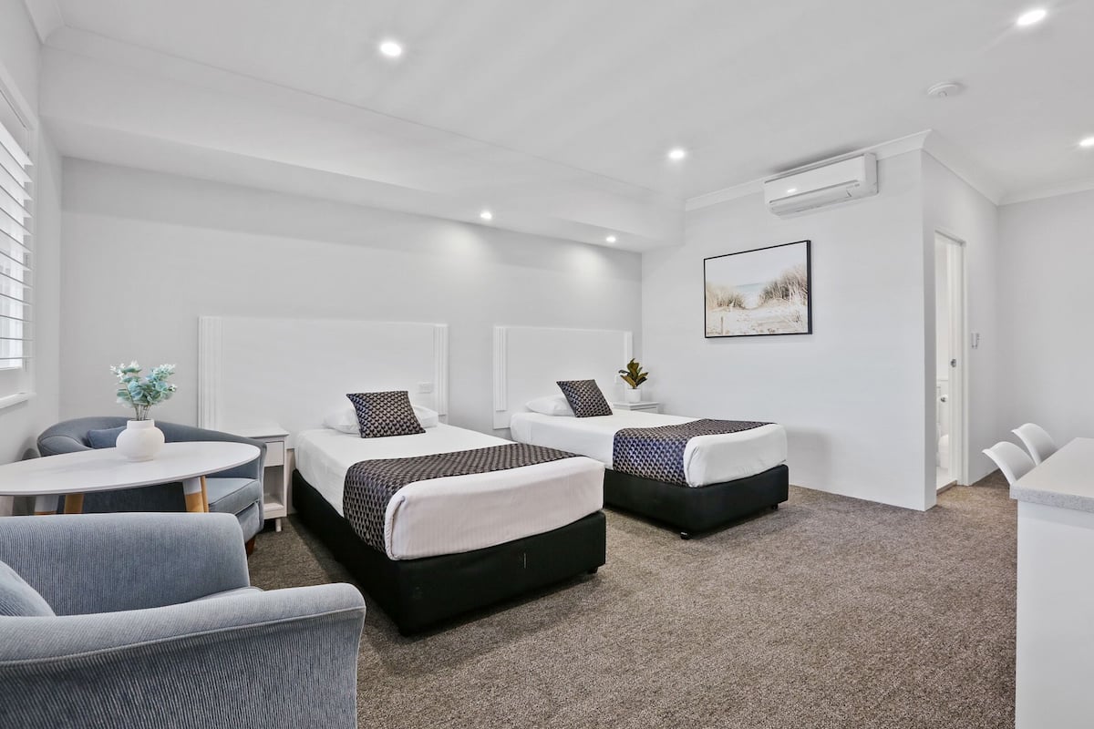Una habitación de hotel moderna con dos camas individuales, un escritorio pequeño, una silla y un sofá.