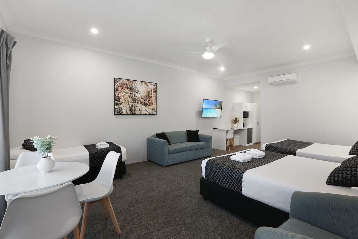 Una habitación de hotel con cama, escritorio, silla, sofá, televisión y ventilador de techo.