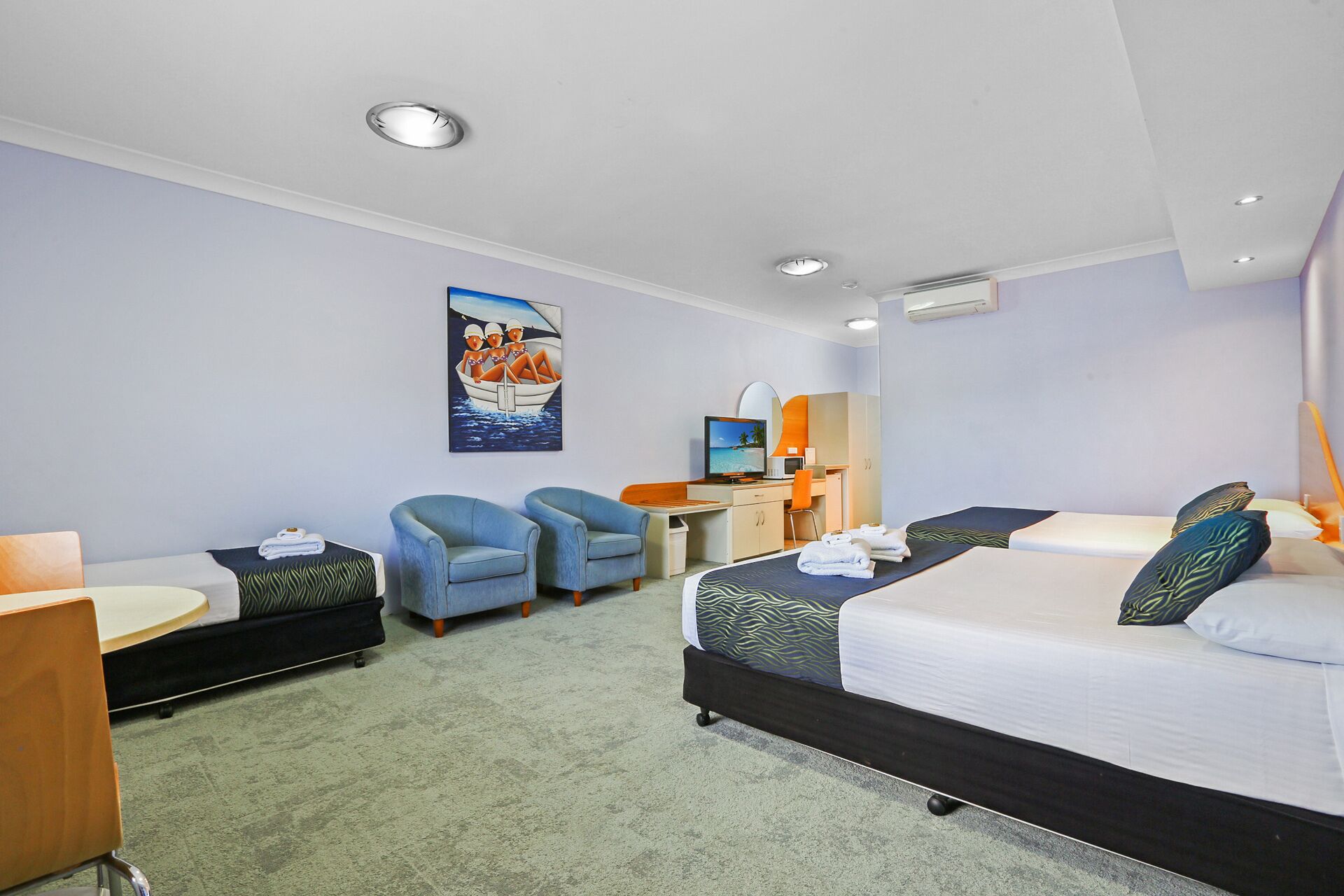 A hotel room with a bed, two armchairs, a desk with a computer, and a painting on the wall.