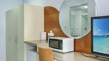 A hotel room with a kitchenette, a microwave, a small refrigerator, a wooden cabinet, a mirror, and a TV displaying a beach view.