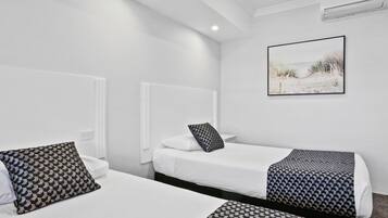 Habitación de hotel con dos camas individuales, ropa de cama blanca, almohadas estampadas, un cuadro en la pared y un equipo de aire acondicionado.