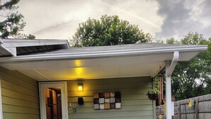 A covered patio with two yellow chairs, a wall-mounted light fixture, and a door leading to a garage.