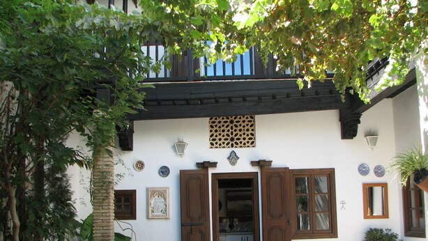 A courtyard with a wooden table, potted plants, and a building with a balcony. - MORISCA DE LA LUNA HOUSE IN GRANADA. PATIO AND GARDEN. (Granada)