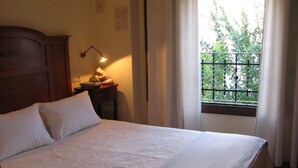 A neatly made bed with white linens, a wooden headboard, a bedside table with a lamp, and a window with a view of greenery. - MORISCA DE LA LUNA HOUSE IN GRANADA. PATIO AND GARDEN. (Granada)