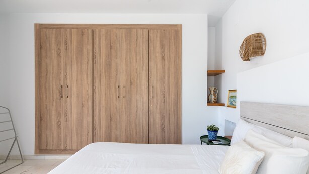 A bedroom with a large wooden wardrobe, a bed with white bedding, and a small bedside table with a plant. - Alfarería Terrace. 2 bedrooms, private terrace (Sevilla)