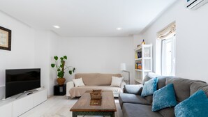 A living room with a flat-screen TV, a beige sofa, a grey sofa with blue cushions, a wooden coffee table, and a bookshelf. - Alfarería Terrace. 2 bedrooms, private terrace (Sevilla)