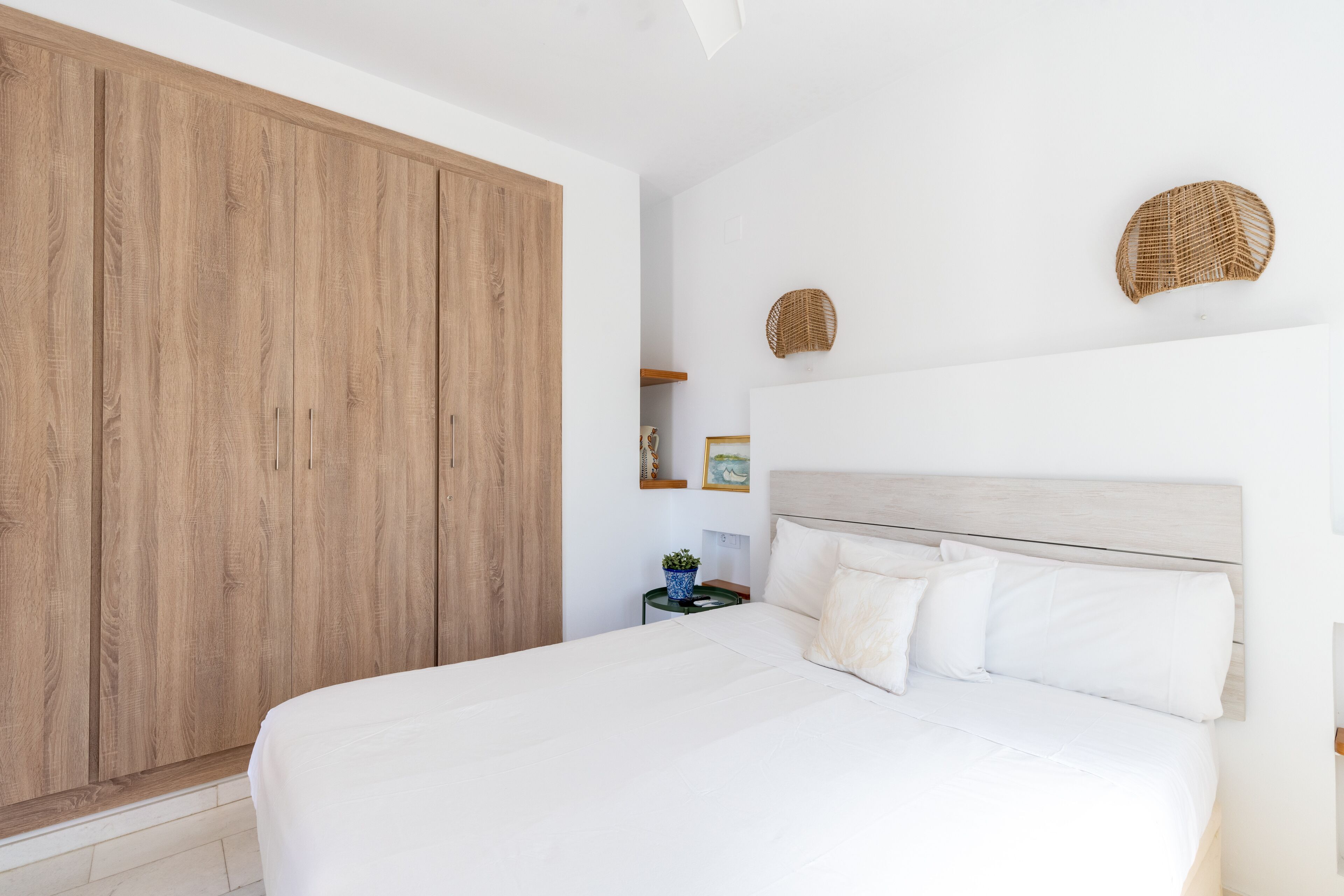 Un dormitorio con un armario grande de madera, una cama con ropa de cama blanca y dos adornos tejidos en la pared.