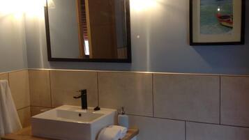 A bathroom with a rectangular sink, a mirror, and a framed picture of a boat on water.